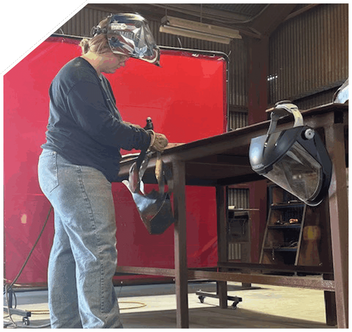 Person welding metal pieces in a workshop with safety gear.