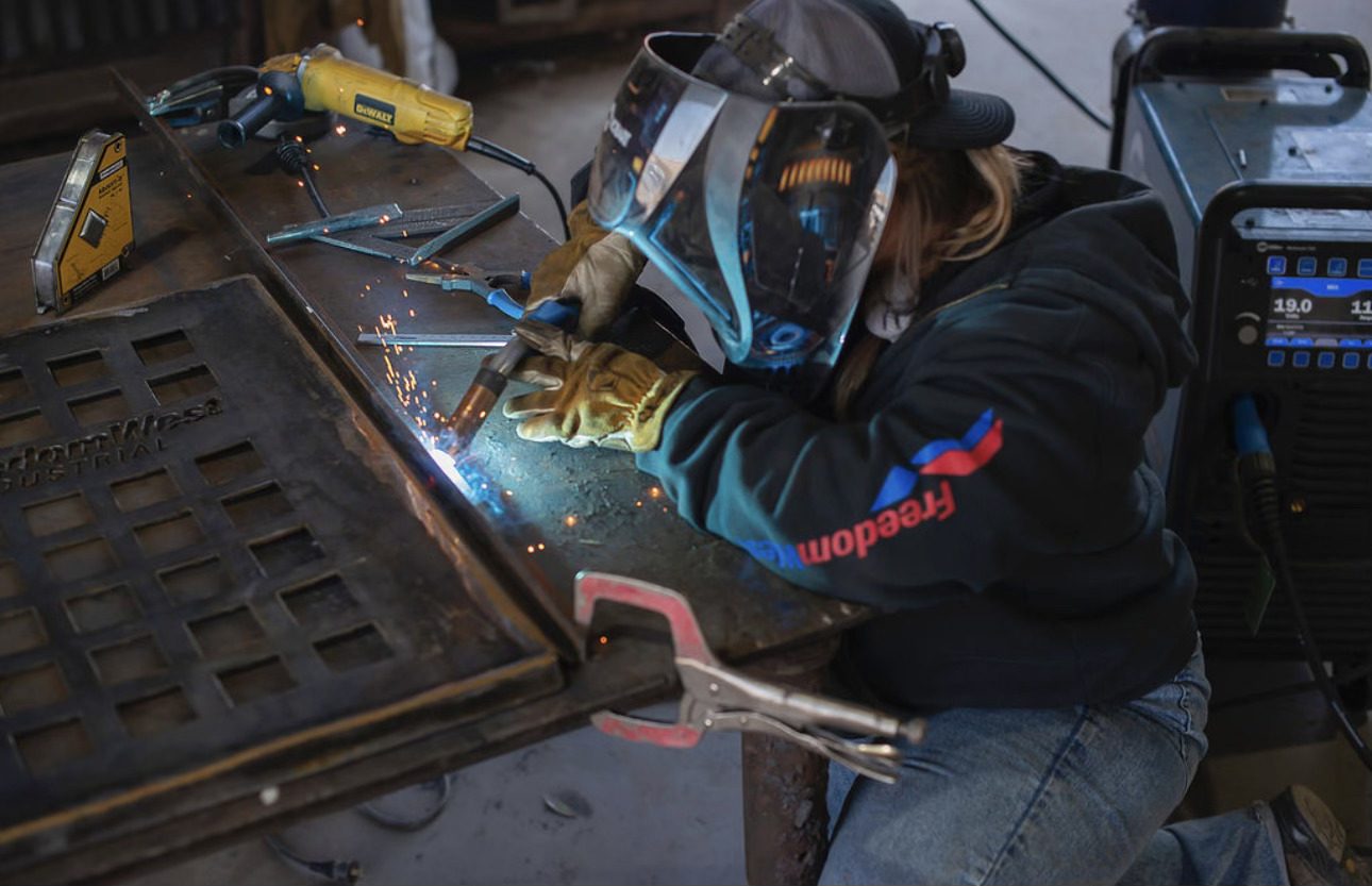 Welder in protective gear welding metal on a workbench.